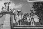 A long shot of children and a nurse standing at the top of a set of stone stairs. Two of the children appear to have their legs, up to their knees, encased in casts Posing on the Front Steps, Circa 1955