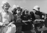 A close up shot of five children leaning on a wooden, horizontal slat, fence. Four of the children are wearing hats. On the Fence, Circa 1955
