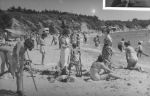 A long shot taken at the beach of adults and children. Two children have crutches and one is standing next to a nurse in uniform. At the Beach, Circa 1955