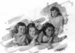 Medium shot of four children on a bed, three are laying prone with arms crossed at the elbow, one child is kneeling on the bed behind the other three all posing for the camera. Portrait of Children, Circa 1955