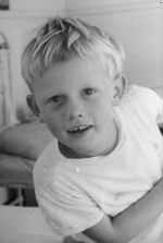 Close up shot of a child sitting on a bed with one arm stretched across the chest posing for the camera. Portrait of a Child, Circa 1955