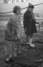 Long shot of three children standing outside, two wearing girl guide uniforms one child's face is obscured by their hands, another has a bandage from below the knee to end of foot with straps across the foot . Brownies, Circa 1955