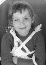 Close up shot of a child wearing a brace secured from shoulder to waist with arms crossed posing for the camera. Portrait of a Child, Circa 1955