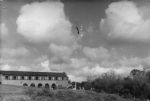Long shot of a building alongside a flagpole with flag, trees to the right of image. Landscape View, Circa 1955