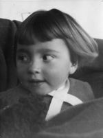 Close up shot of a young child who is looking to their right. The child has a ribbon around their neck that is crossed over, on top of a jumper. Portrait of a Child, Circa 1955