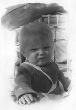 Close up shot of an infant seating in bed with braces across shoulder to waist posing for the camera. Portrait of a Child, Circa 1955