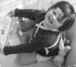 Medium shot of a child seated outside with braces strapped across from neck to chest holding a board a doll is alongside, posing upwards towards the camera. Playing, Circa 1955