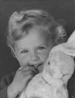 Close up of a child holding a toy bunny fingers in mouth posing for the camera. Portrait of a Child, Circa 1955