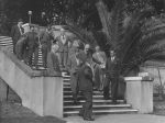 Long shot taken outside of a group of men standing and walking down a concrete and brick set of stairs. There is a huge palm to the right of the stairs. Uncle Bobs Club on the Front Steps, Circa 1955