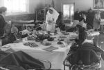 Long shot of children around a party table. Some are in chairs and others are in beds pulled close to the table. There is party fare and flowers on the table and they are wearing party hats. There is a nurse serving drinks from a jug. Birthday Celebrations at the Hospital, Circa 1955
