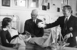 Medium shot of a patient lying on a metal framed bed. The left leg is in traction with a metal pulley system at the end of the bed. There are two men standing beside the bed in suits. One man's jacket has a monogram on the pocket. Uncle Bobs Club Visiting, Circa 1955