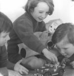 Close shot of three children sitting and lying on the ground playing with a toy jeep. One child is holding a doll. Play Time, Circa 1955