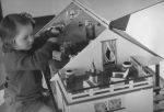 Medium shot of a young child sitting on the ground playing with a dolls house. The lid is lifted so that you can see the rooms inside. Play Time, Circa 1955