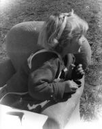 Medium shot of a young child facing away from the camera sitting in a small lounge chair outside on the grass. Portrait of a Child, Circa 1955