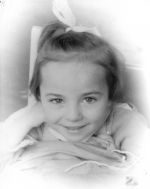 Close frontal shot of the face a young child smiling at the camera with a bow in the ponytail at the top of the head. Portrait of a Child, Circa 1955