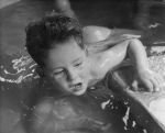 Close shot of a young patient lying in water holding onto the side for support. In the Pool, Circa 1955