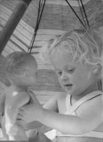 Close shot of a young child sitting under a beach umbrella playing with a doll. Play Time, Circa 1955