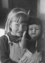 Close shot of a child facing the camera holding a large doll so that it also faces the camera. The child is missing a front tooth. Play Time, Circa 1955