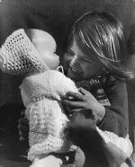 Mid shot of a child seated smiling holding a baby doll. Child and Doll, Circa 1955