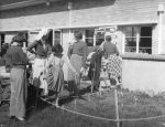 Long shot of a group outside of a building standing around a garden plot. There is a child in crutches and a nurse. Greeting Visitors, Circa 1955