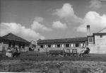 Long shot of the outside of a building. In the foreground are people sitting on garden seats. Exterior View of Hospital, Circa 1955