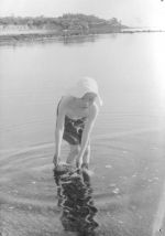 Long shot of a child wearing a sunhat and shorts paddling in the sea. Playing in the Sea, Circa 1955