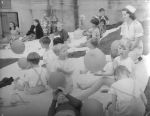 Long shot of a number of children and nurses sitting outside on blankets on the grass. Some of the children are playing with balloons. Celebrations on the Lawn, Circa 1955