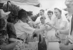 Long shot of ladies selling drinks to nurses and children from a stand outside under an umbrella. At the Races, Circa 1955
