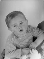 Close shot of a young child wearing a knitted jumper, sitting on the lap of a person out of the picture. Portrait of a Child, Circa 1955