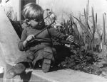 Long shot of a child sitting outside on a concrete ledge playing with a stick and a cymbal. Child Playing Outside, Circa 1955