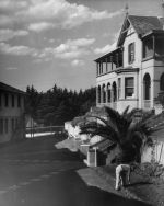 Long shot of the front of a building. There is a man bent over working in the garden in the foreground. Exterior View of the Hospital, Circa 1955