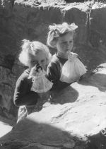 Medium shot of two young children standing behind a stone fence holding Barbie dolls. Children Playing, Circa 1955