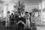 Long shot of a children's ward. In the centre is a tall Christmas tree. In front is Father Christmas seen from behind bending down. There are a number of nurses standing around helping him. There are parents and children in beds in the background. Father Christmas at the Hospital, Circa 1955