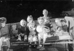 Long shot of ten children seated on a bed in front of a small brick wall posing for the camera. Children Lined up on a Bed, Circa 1955