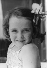 A close up shot of a young child, smiling for the camera. The child has dark chin length wavy hair. Portrait of a Child, Circa 1955
