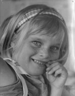 A close up shot of a young child smiling for the camera. The child is wearing a head band. Portrait of a Child, Circa 1955