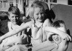 Medium shot of three children seated on a bed outside posing for the camera. Children Outside, Circa 1955