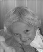 A close up shot of a young child looking at the camera. Child has short fair hair. The bars of a bed are just visible in the foreground. Portrait of a Child, Circa 1955