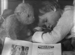 A close up shot of a young child asleep. Child has a teddy next to their head and a book open next to their arm. Bed Time, Circa 1955