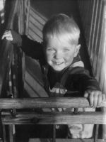 A close up shot of a young child looking at the camera. Child is standing holding on to timber railing on both sides. Portrait of a Child, Circa 1955
