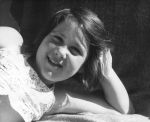 Medium shot of a child laying prone on a blanket with arm bent at elbow with hand holding face posing for the camera. Portrait of a Child, Circa 1955