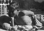Medium shot of a child outside laying prone on a bed with arm bent at elbow hand holding his head other arm stretched over back trees in the background posing for the camera. Outside on the Balcony, Circa 1955