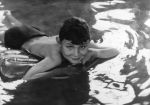 Medium shot of a child laying prone on a flotation device in a pool posing for the camera. In the Pool, Circa 1955