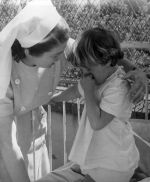 Medium shot of a nurse comforting a child kneeling on a bed. Comfort from the Nurse, Circa 1955