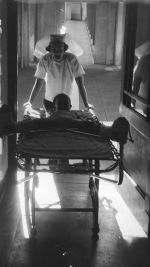 Long shot of a nurse pushing a bed down a corridor. On the bed is a small child with legs spread wide due to wearing a leg brace. Riding Through the Corridors, Circa 1955