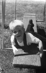 Medium shot of a child outside lying on a piece of play equipment. The photograph is taken front on. Playing Outside, Circa 1955