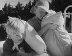 Medium shot of two children outside on a bed cuddling pillows. Posing for the Camera, Circa 1955