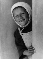 Close shot of a young child peering around a corner. The smile shows one tooth missing and there is a bandage covering the head. Smiling Child with Cast, Circa 1955