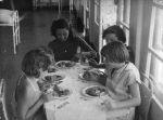 Medium shot of a woman sitting at a small table with four children, all eating their dinner. Dinner Time, Circa 1955