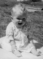 Close shot of a laughing baby sitting on a blanket on the grass outside. Smiling Infant, Circa 1955